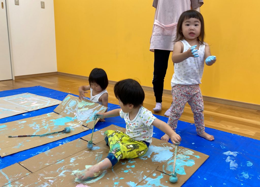 3人の子どもたちが大きなダンボールに思い思いの絵を描いて表現している様子